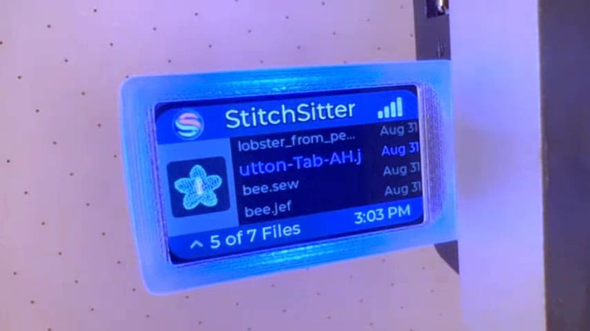 A StitchSitter dongle showing its identity colour on the screen and on the light along its edge